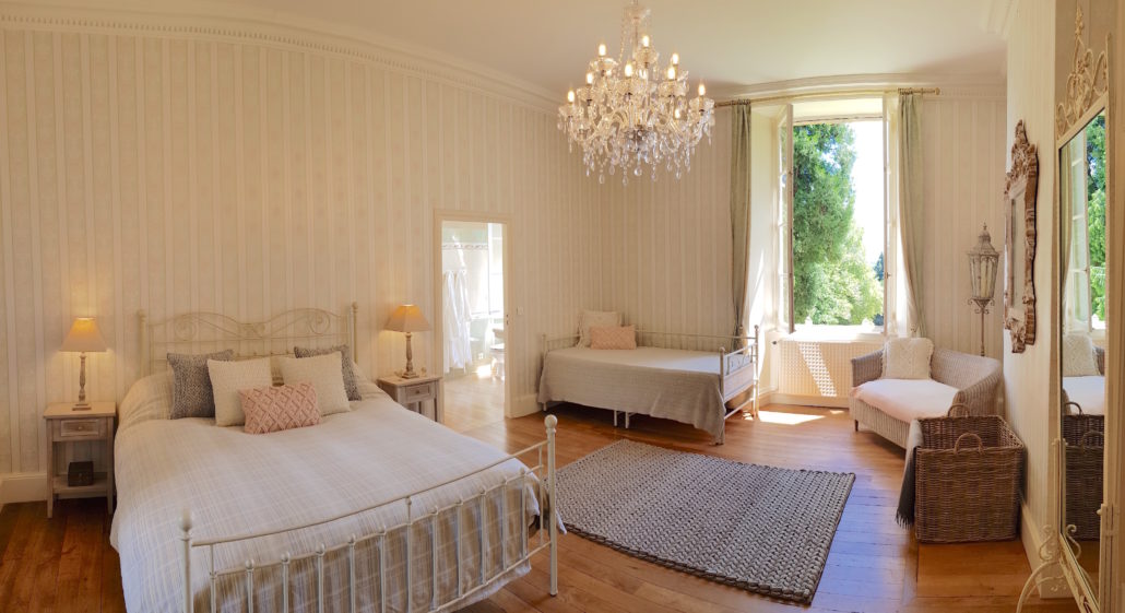 Large neutral bedroom with chandelier and garden view